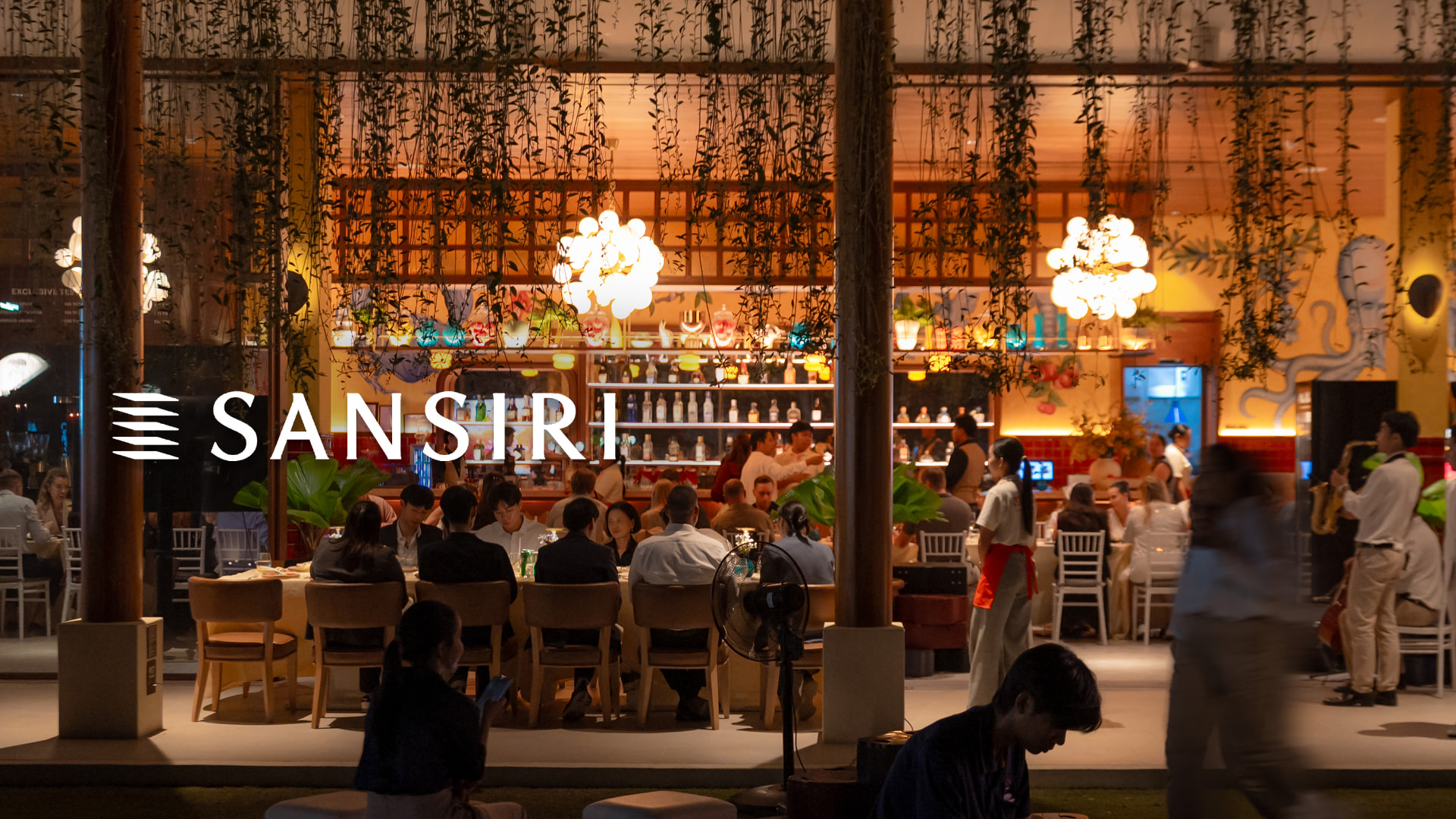 Sansiri New Year Dinner — evening restaurant terrace with guests dining under hanging plants, carrying the SANSIRI logo