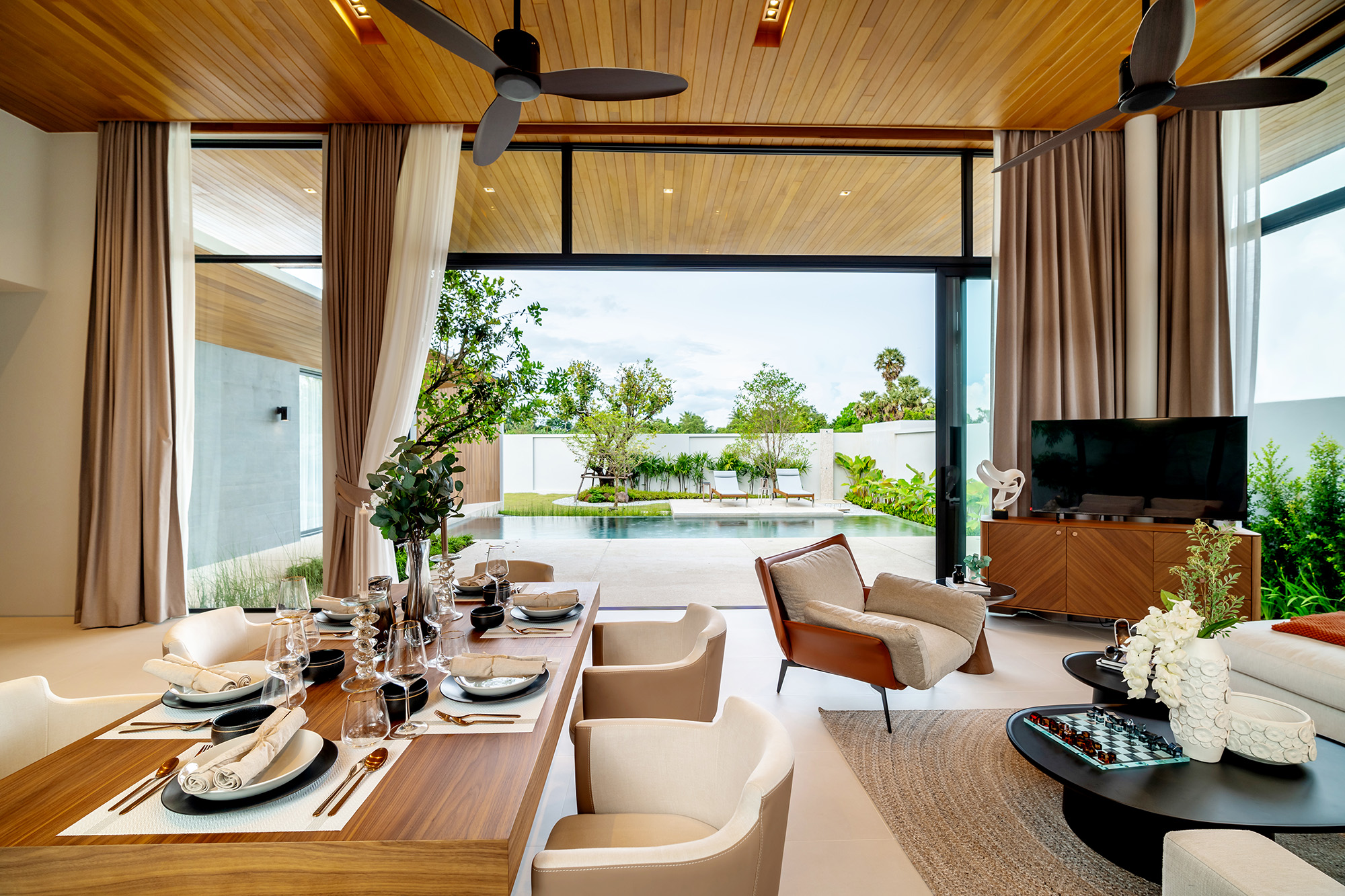 Botanica Four Seasons — dining table and living room opening through glass doors onto the pool and garden