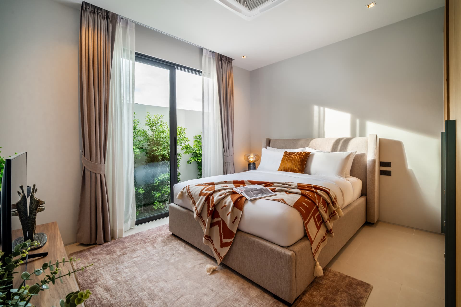 Botanica Four Seasons — bedroom with an upholstered bed, an amber accent pillow and glass doors onto a planted courtyard