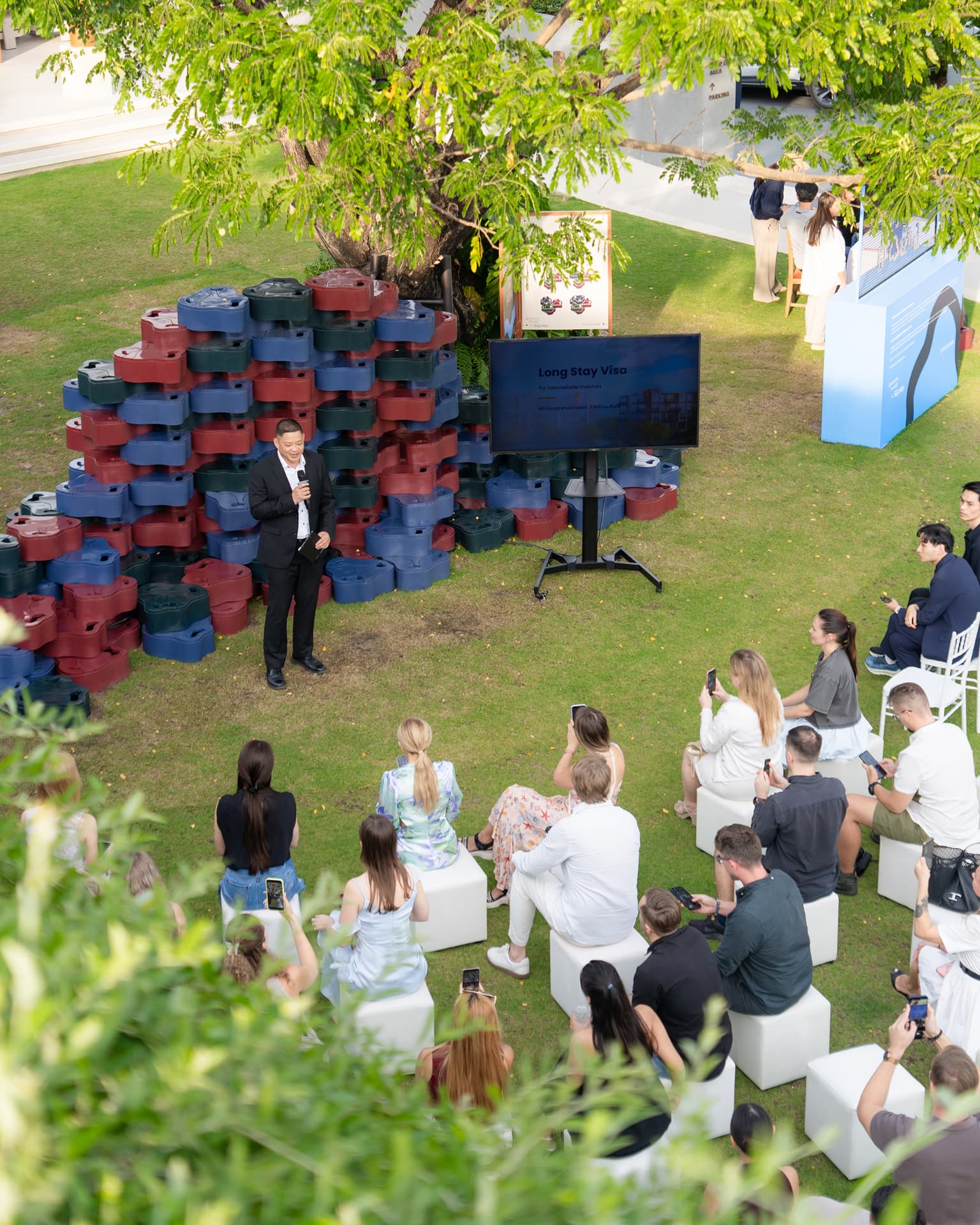 Sansiri New Year Dinner — aerial view of a lawn seminar with a speaker, screen and seated guests under a tree