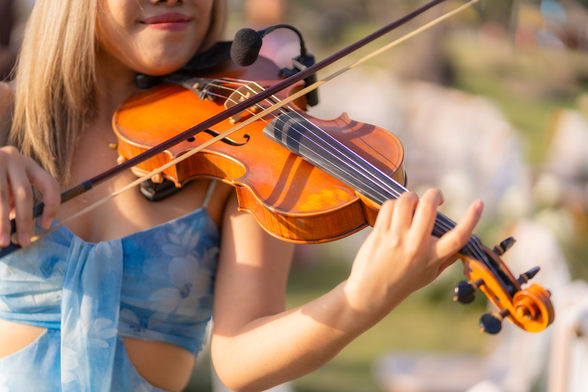 Wedding Setup — violinist in a pale blue floral dress playing an amber violin fitted with a clip-on microphone