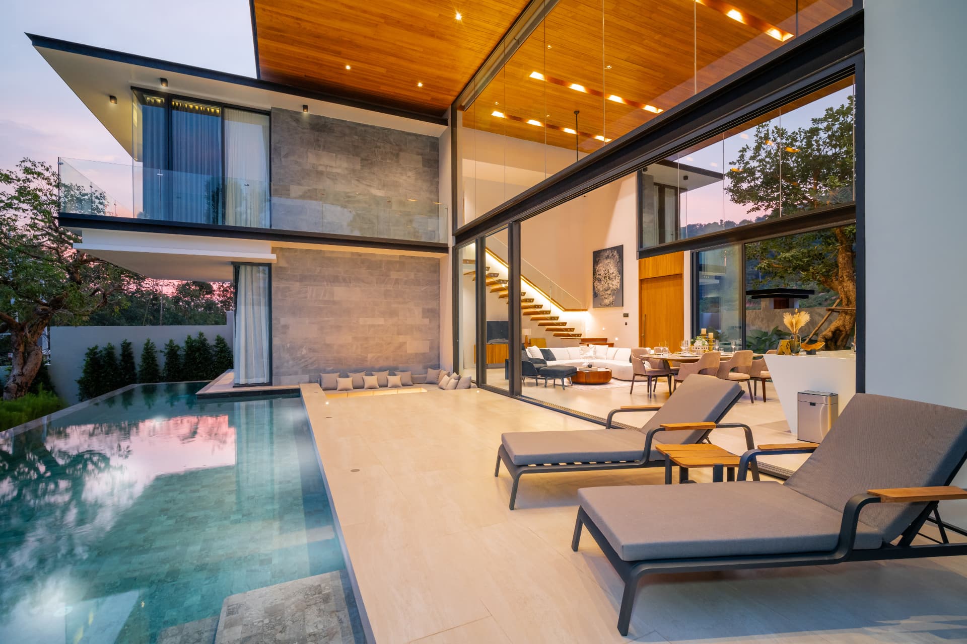 Botanica Foresta II — pool terrace at dusk with loungers facing the glass-walled living room