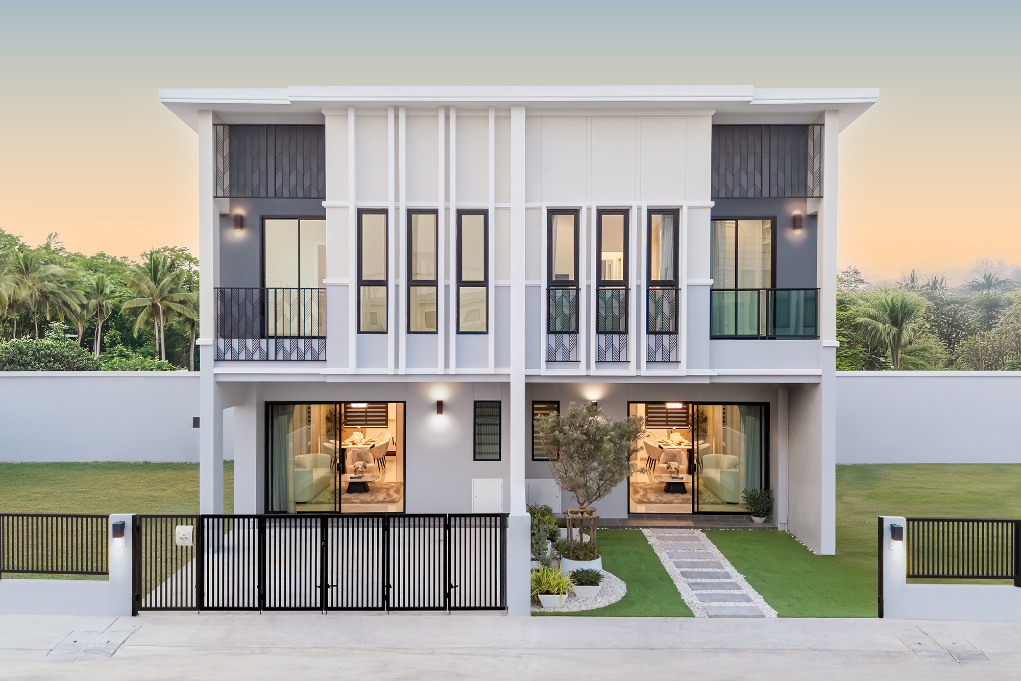 K Avenue II — twin two-storey villas with lawns, a paved carport and palm trees at dusk