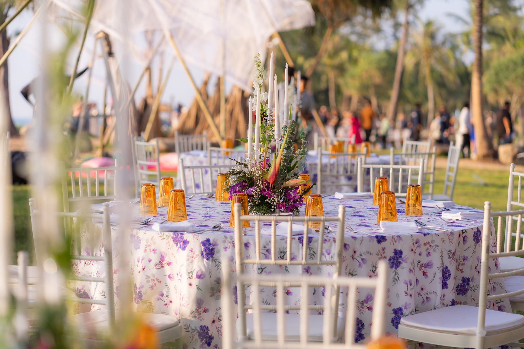 Wedding Setup — round banquet table on the lawn with purple floral linen, amber tumblers and a tall candle centerpiece