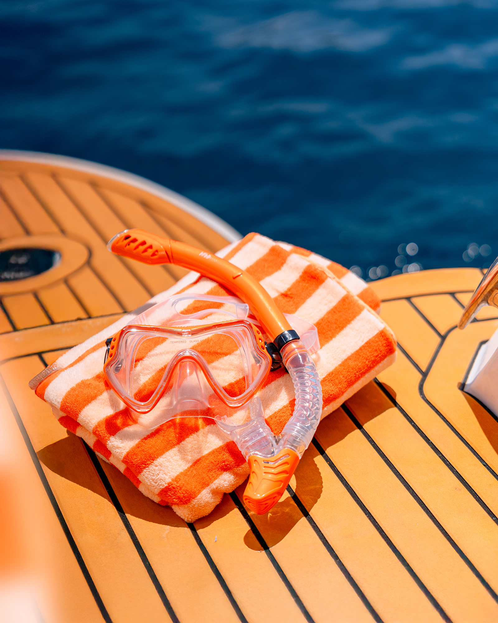 Once Yachting — orange diving mask and snorkel resting on a striped towel atop teak decking