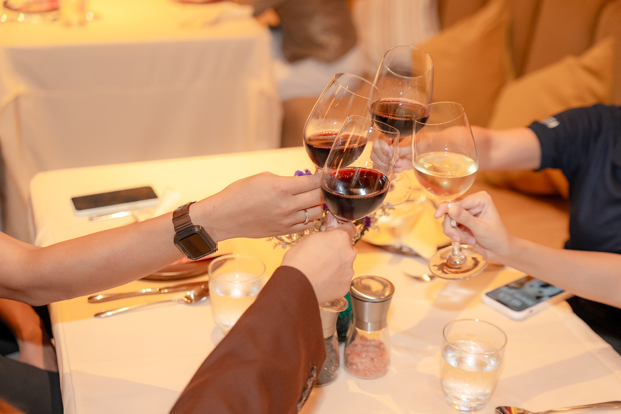 Sansiri New Year Dinner — hands raising glasses of red and white wine over a candle-lit dinner table