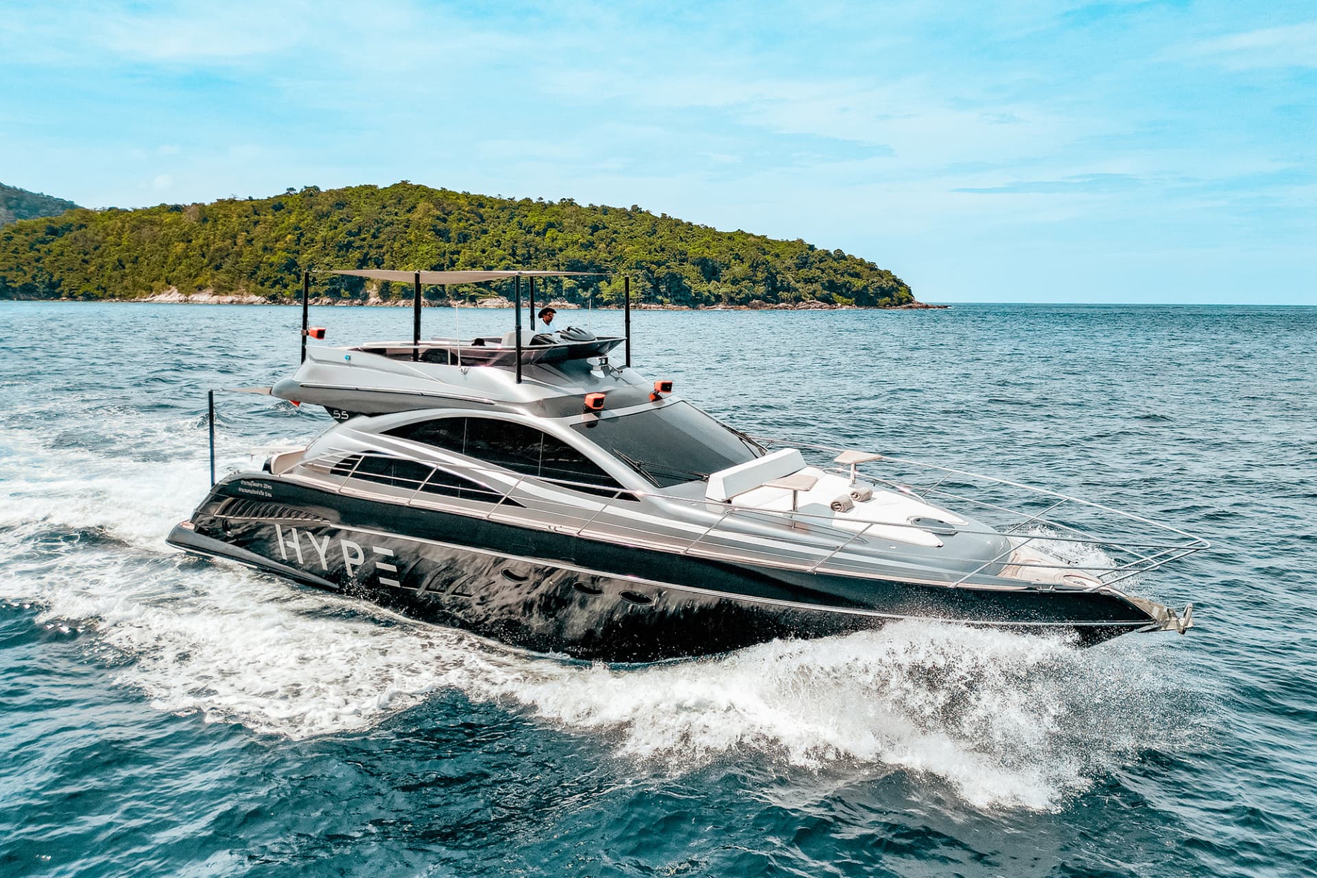 Hype Yacht — the grey motor yacht cruising past a green island with HYPE lettering on the hull, seen from ahead