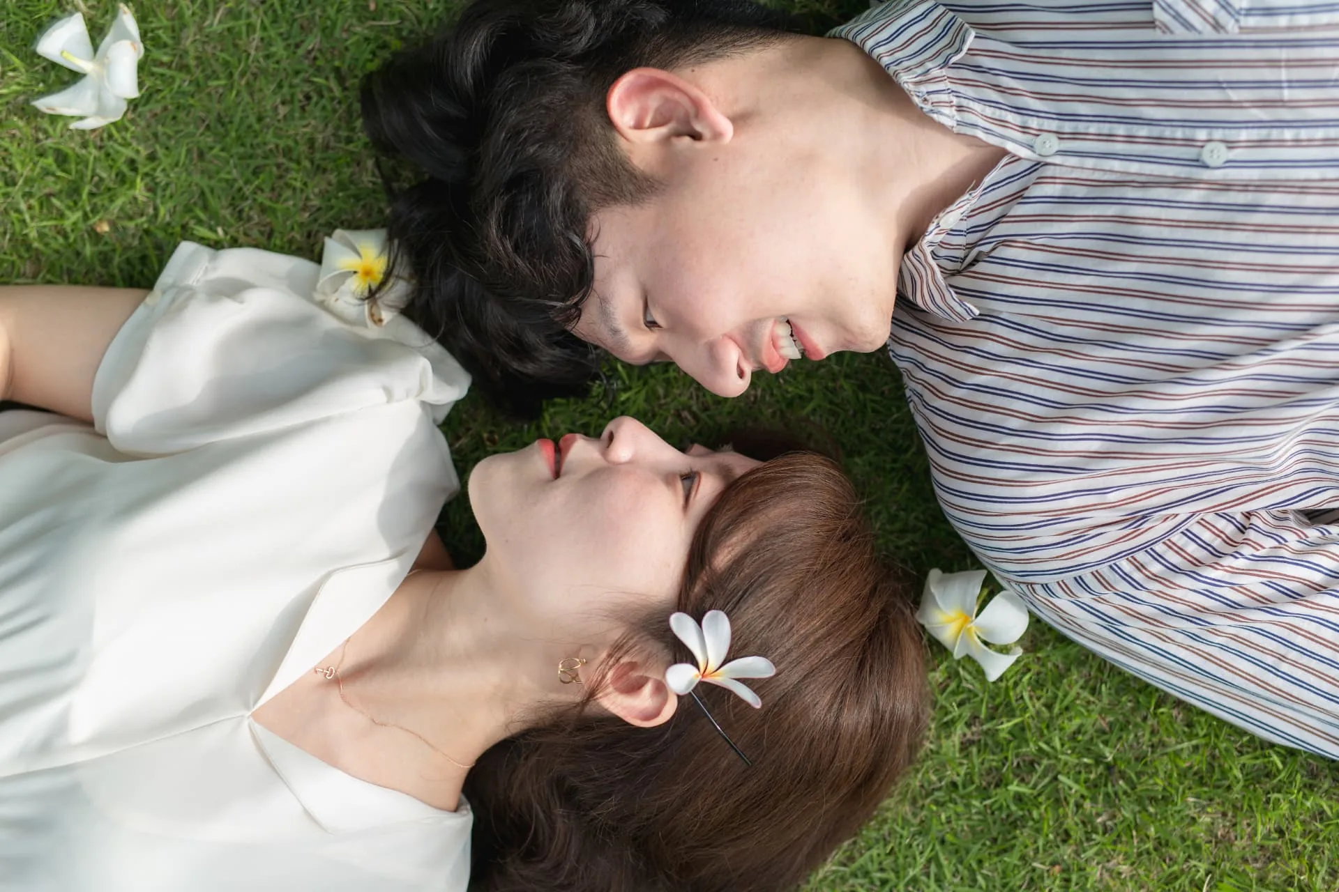 Couple lying head to head on the grass with plumeria blossoms — ภาพคู่รักและช่วงเวลาร่วมกัน
