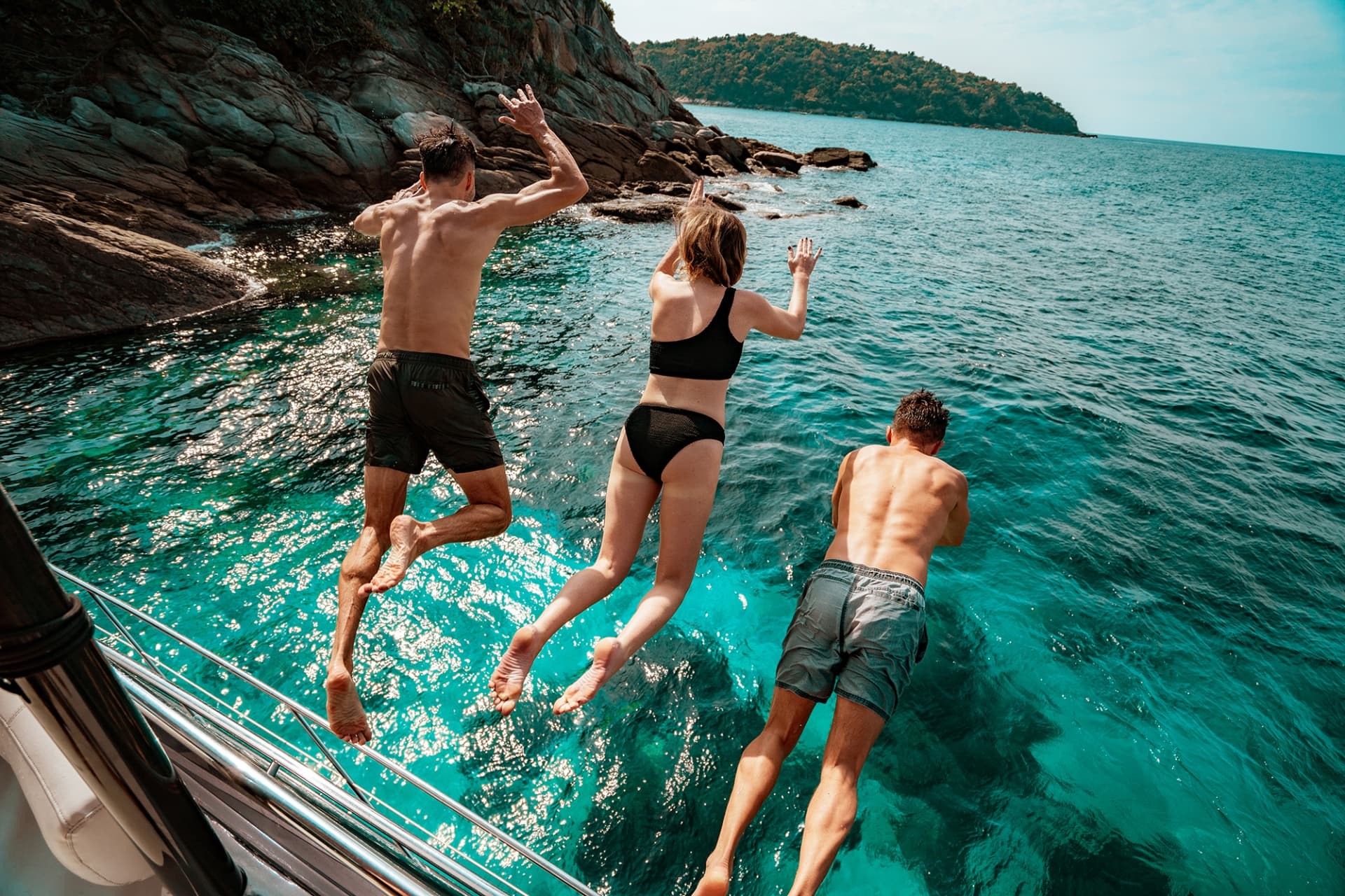 HYPE YACHT — guests jumping off a yacht into a rocky turquoise cove