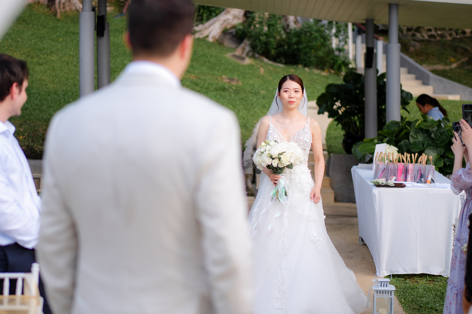 Thomas & Jane The Wedding — bride walking toward the groom past a welcome table as guests gather
