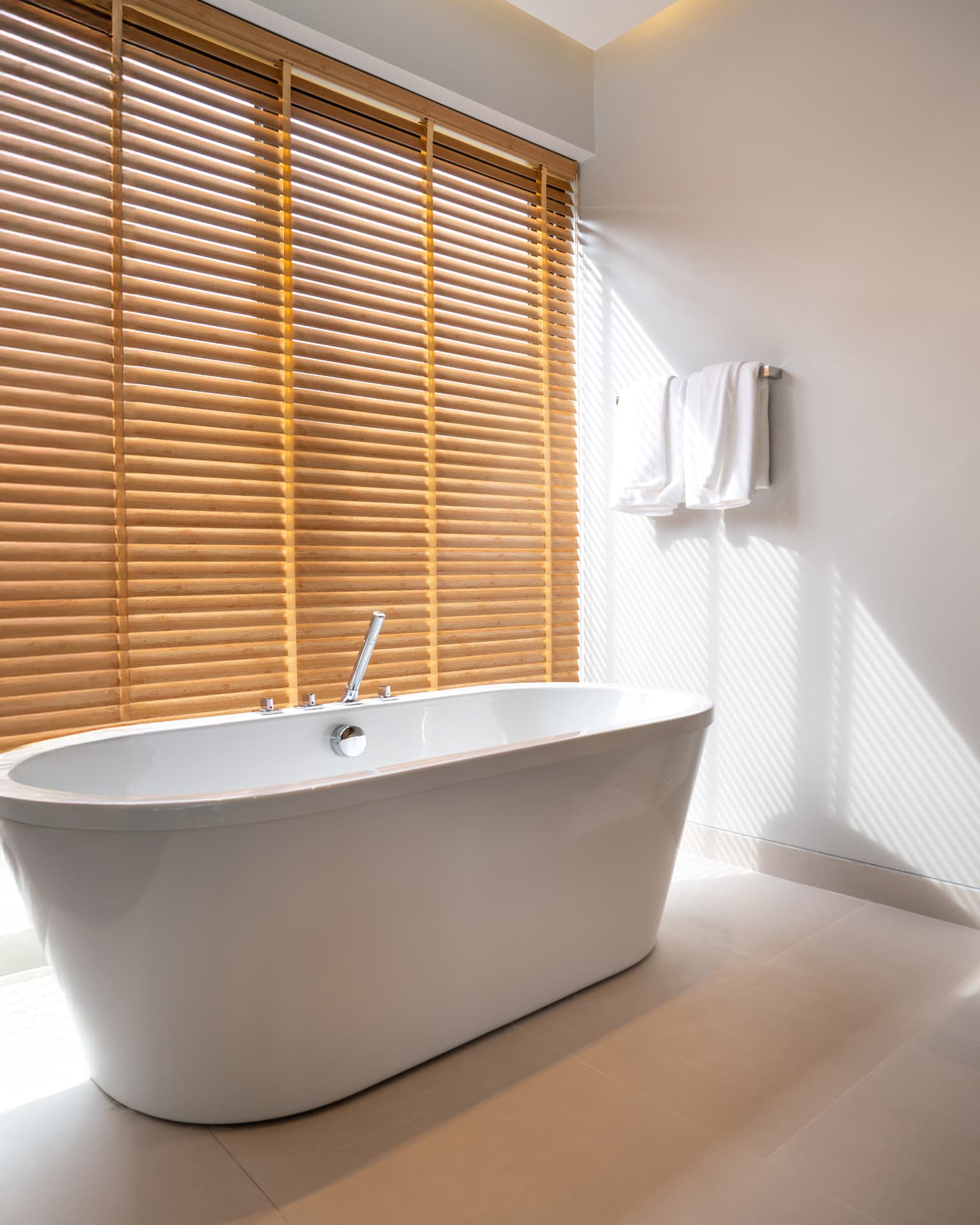 Botanica Four Seasons — soaking tub beside wooden blinds casting slatted light