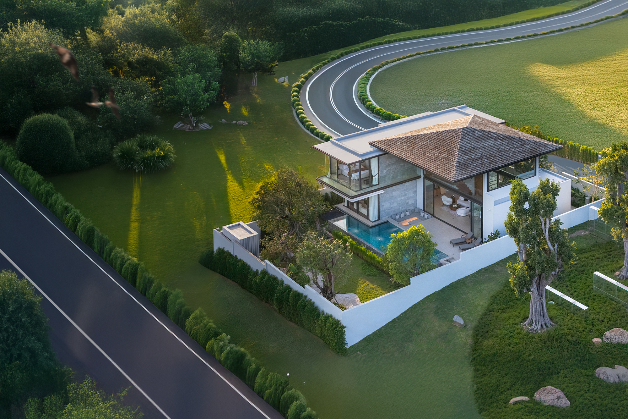 Botanica Foresta II — aerial view of the villa and pool beside a curving road at golden hour