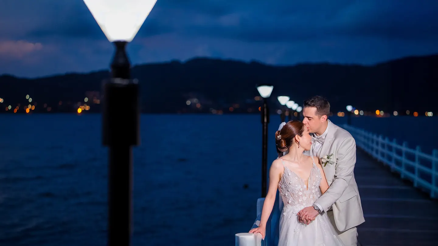 Thomas & Jane The Wedding — couple on a lamp-lit pier at night, groom kissing the bride's forehead over deep blue water — ภาพงานแต่งงานและคู่บ่าวสาว