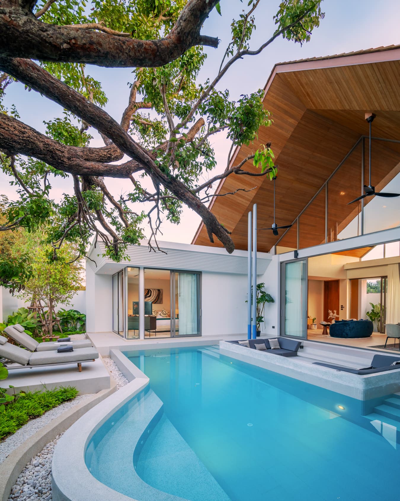 Botanica Louvre — curved pool beneath a tree beside the timber-roofed villa
