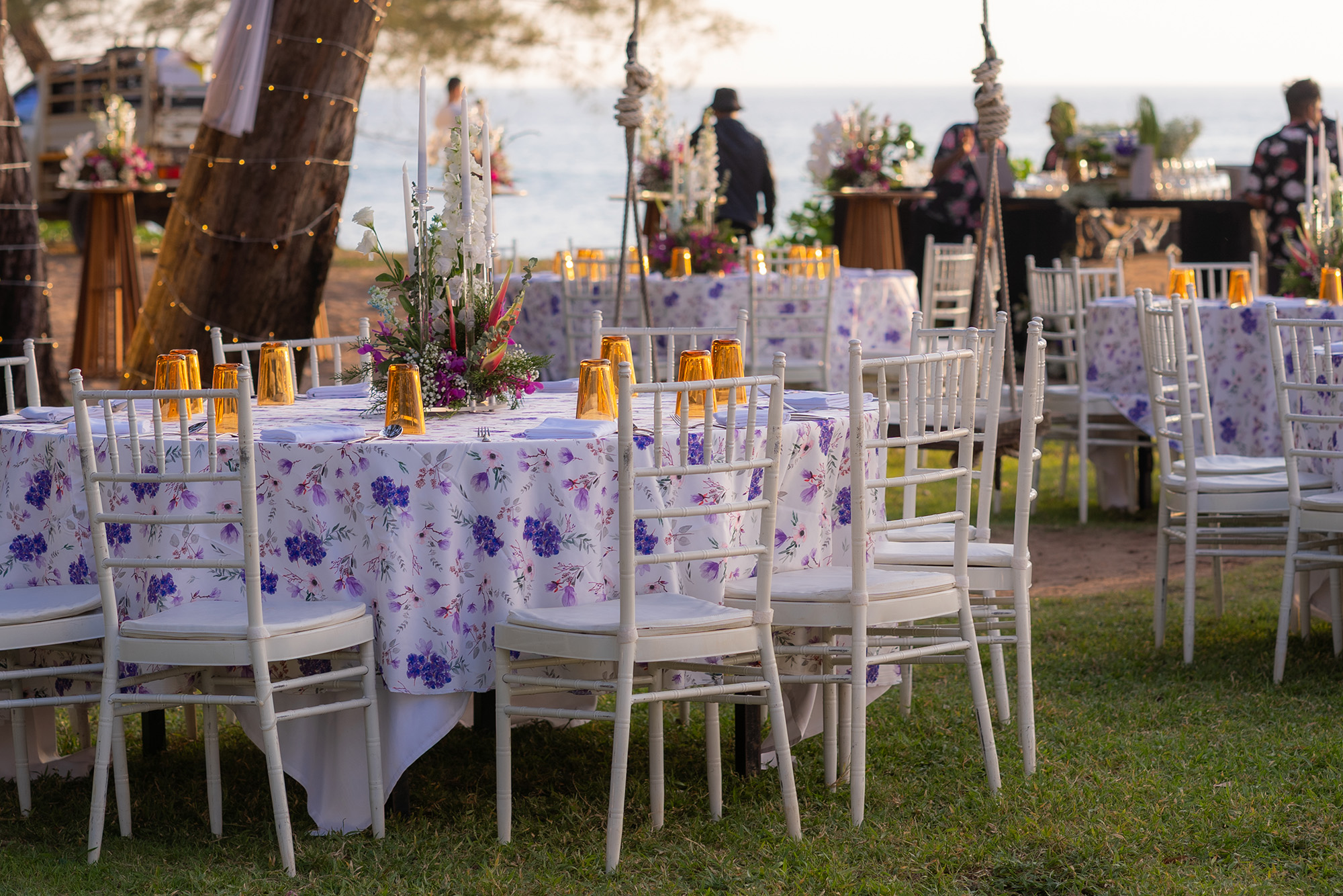Wedding Setup — dining tables facing the sea at dusk, trees wrapped in fairy lights behind them