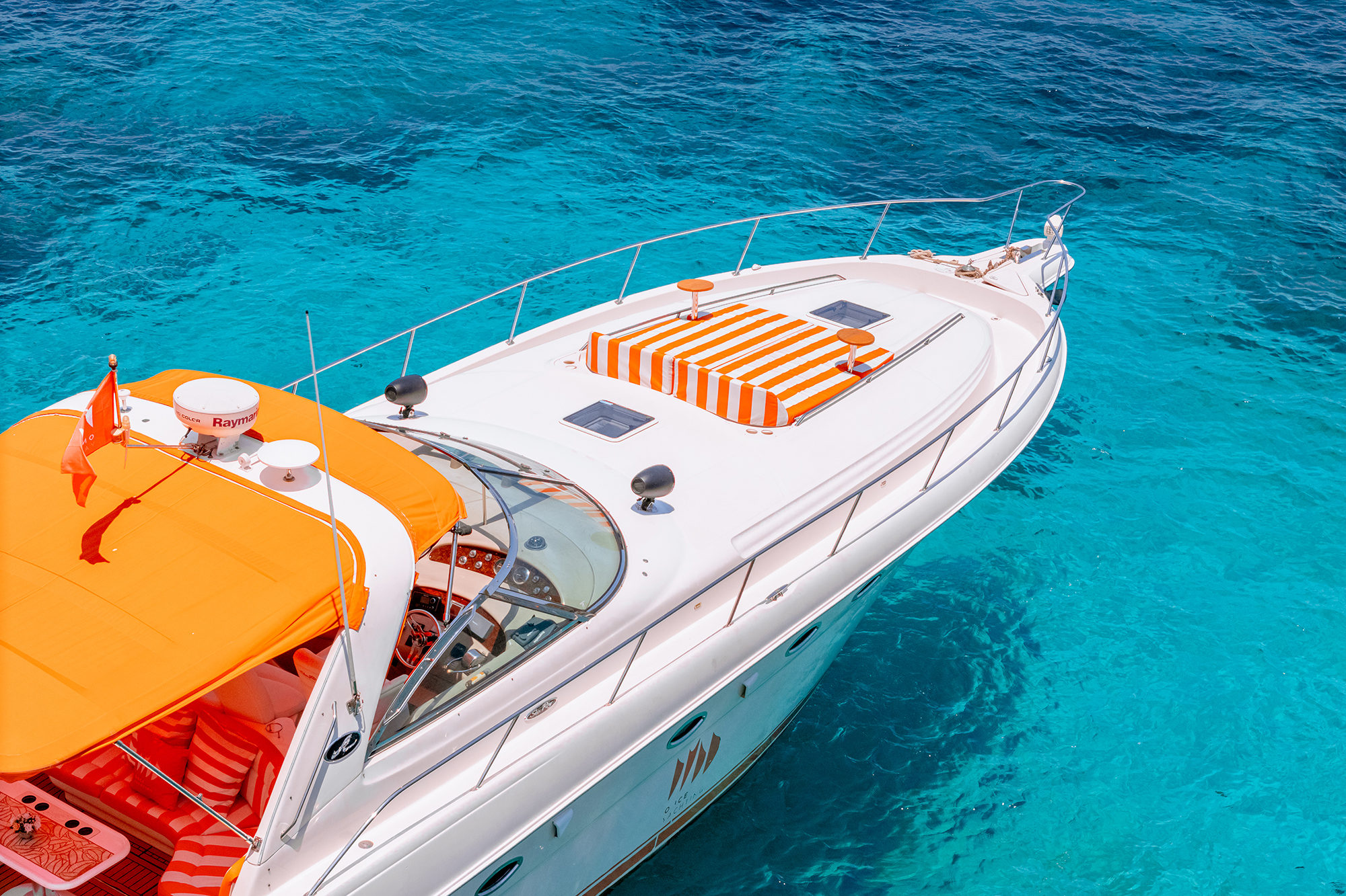 Once Yachting — high-angle view over the bow and cockpit with an orange bimini and striped sun cushions on turquoise water