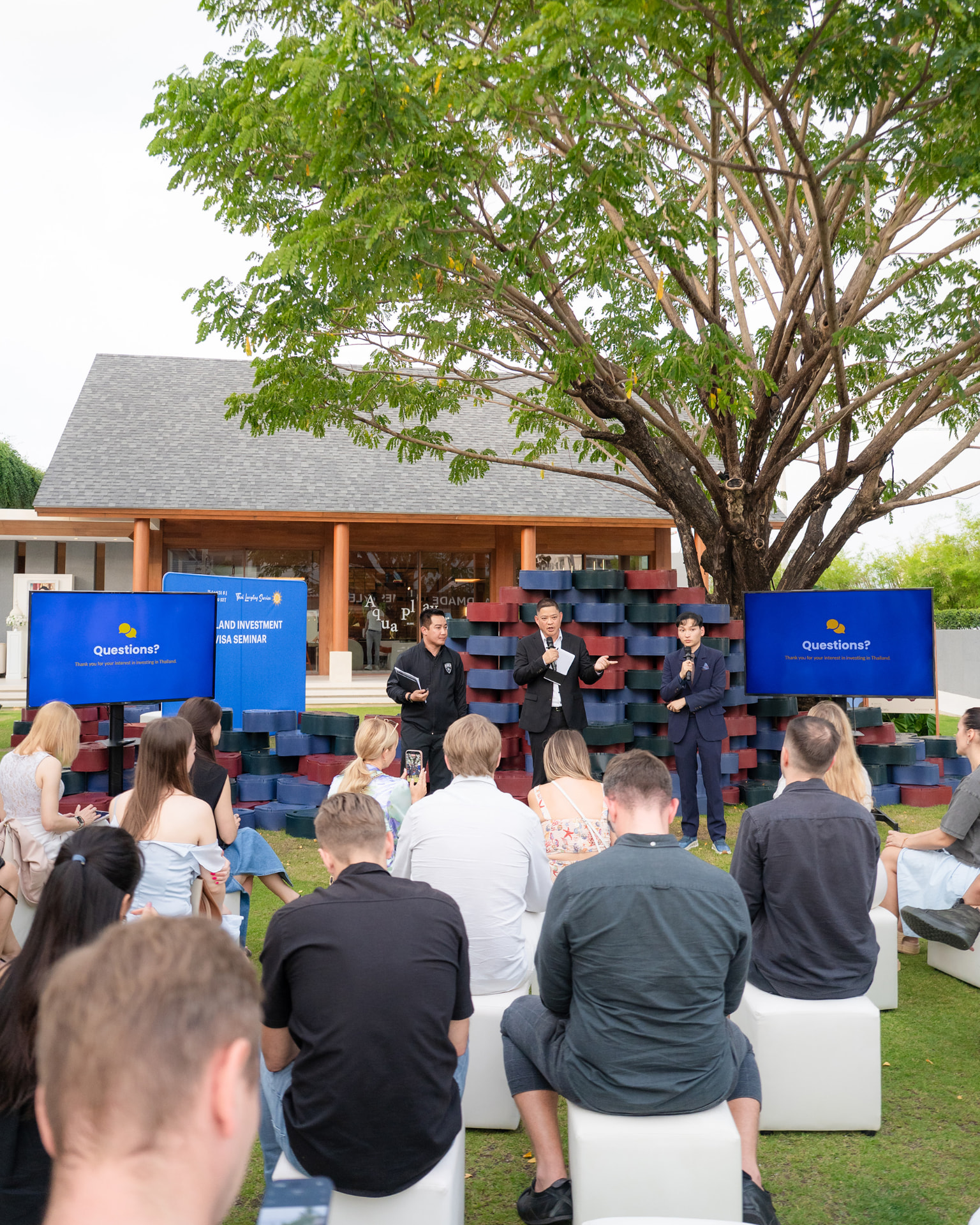 Sansiri New Year Dinner — two speakers presenting under a large tree to seated guests on a lawn