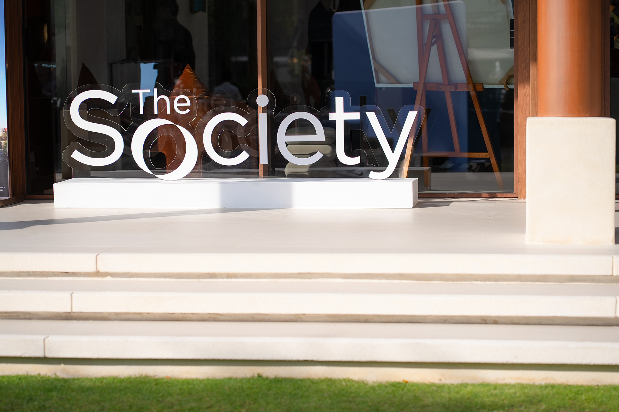 Sansiri New Year Dinner — The Society lettering sign in sunlight by a glass entrance on a bright lawn